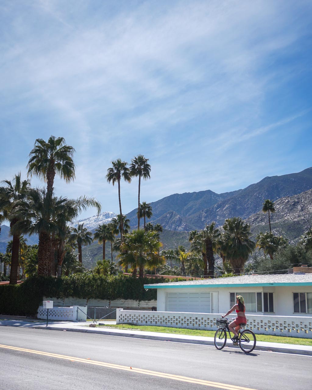 A young woman biking along the street with palm trees and mountain views