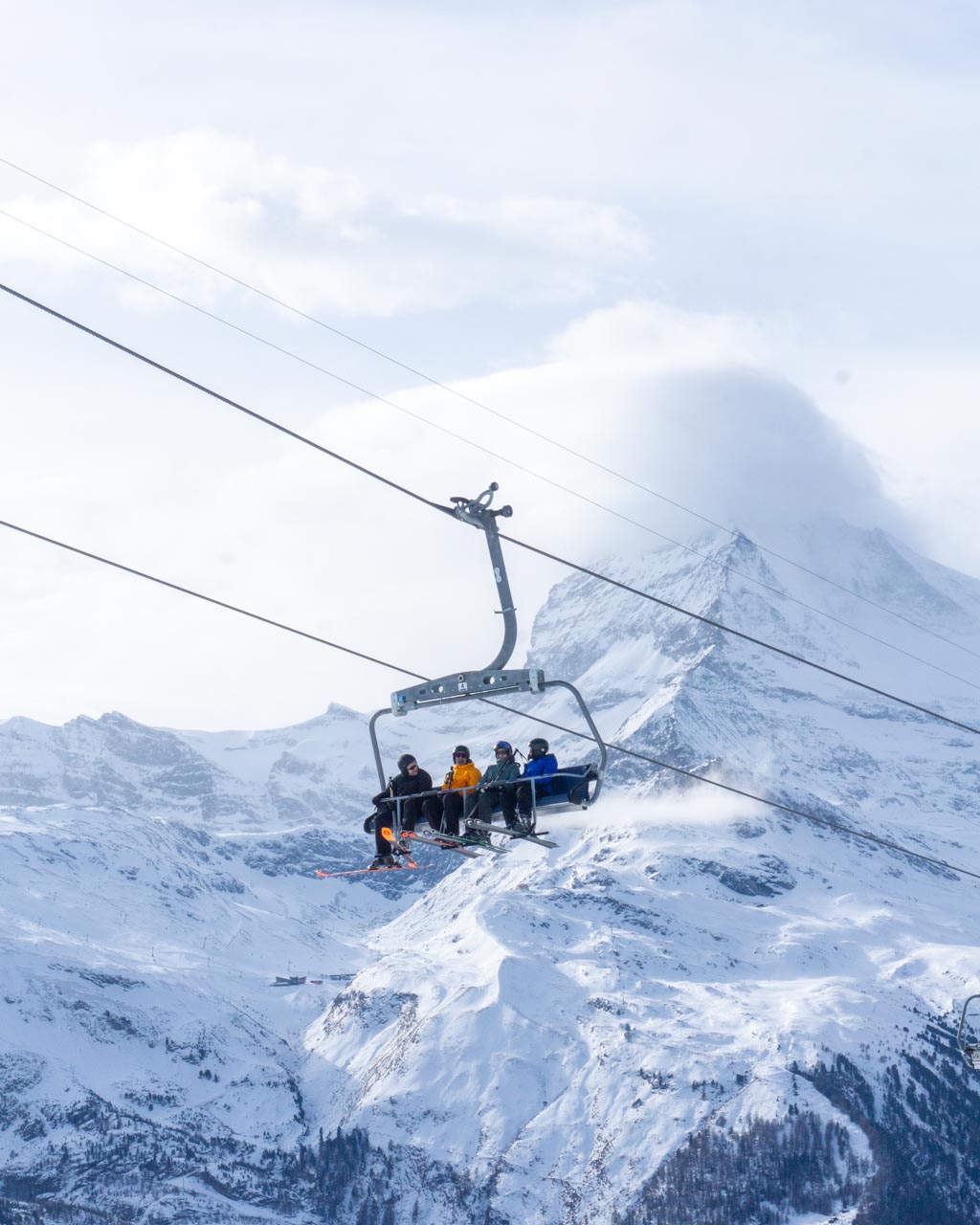 A ski lift holding four skiers in a wide shot in Zermatt